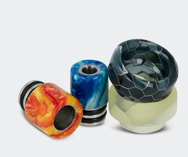 Four drip tips for vaping devices, in different sizes and colours, on a grey background.