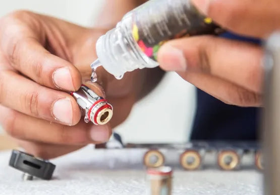 Showing someones hands priming a vape coil by putting a few drops of e-liquid of the cotton windows of the coil.