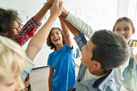 Happy diverse multiethnic kids junior school students group giving high five together in classroom.