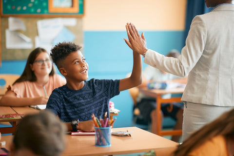Happy elementary student and his teacher greet with high five gesture during class at school.