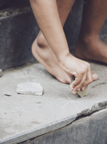 A little child perched over on a broken step, creating art with chalk on a summer day. 