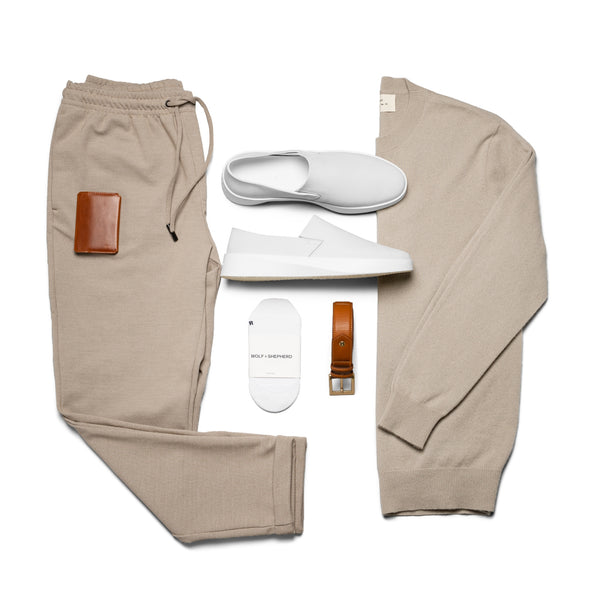 White leather slip-on shoes laid out on table overhead with socks, pants, and a jacket.