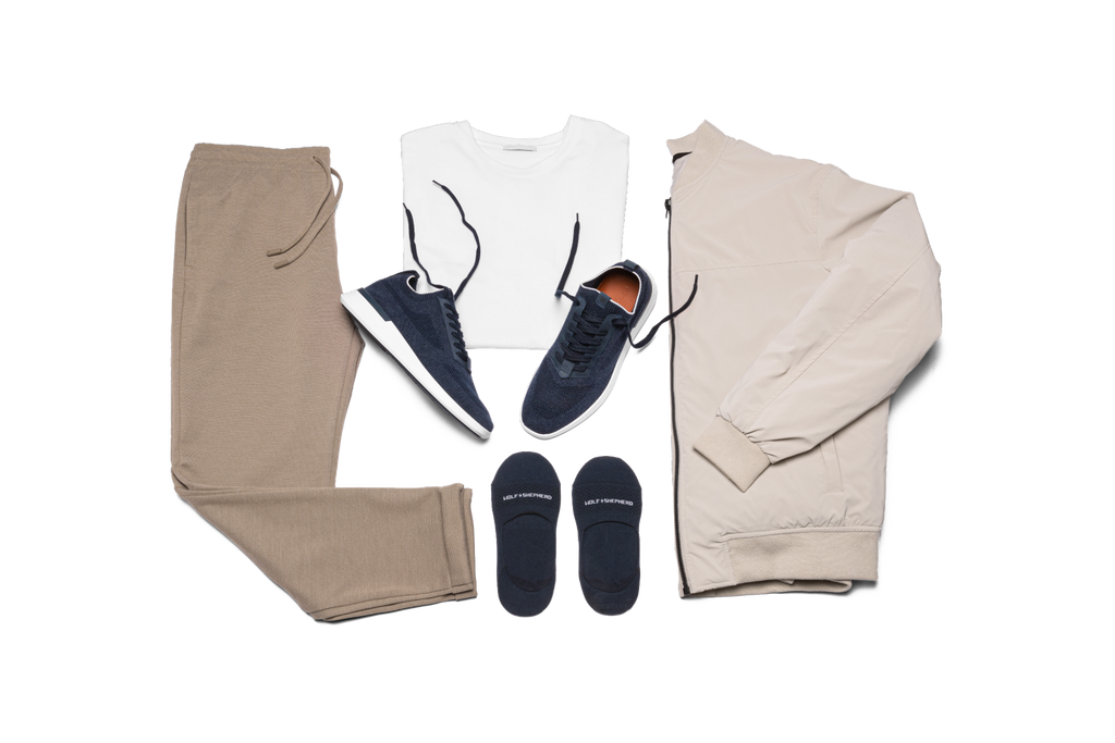 Navy shoes laid out on a white surface with socks, pants, a jacket, and a shirt. 