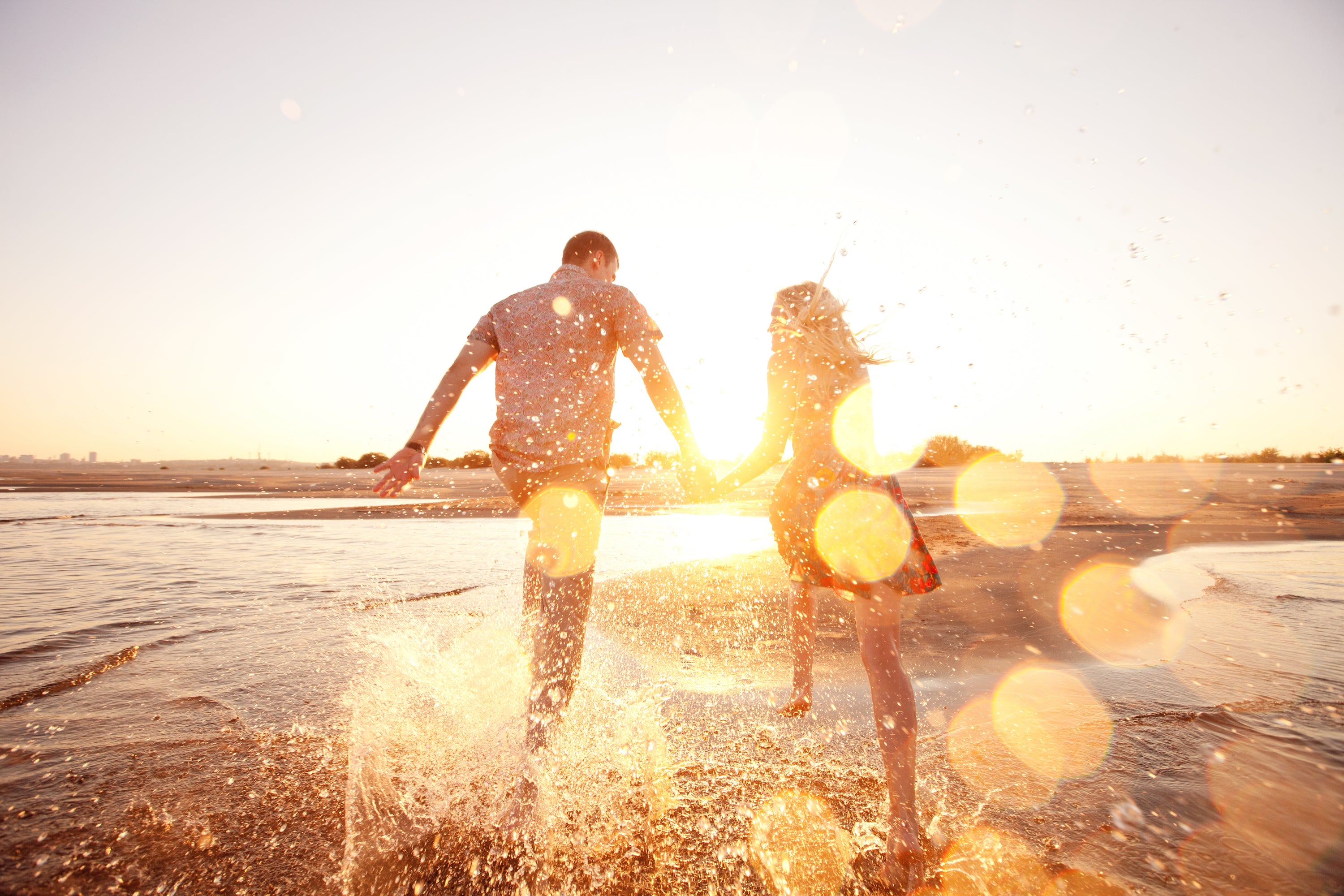 man and woman holding hands running through shallow ocean water in sunshine
