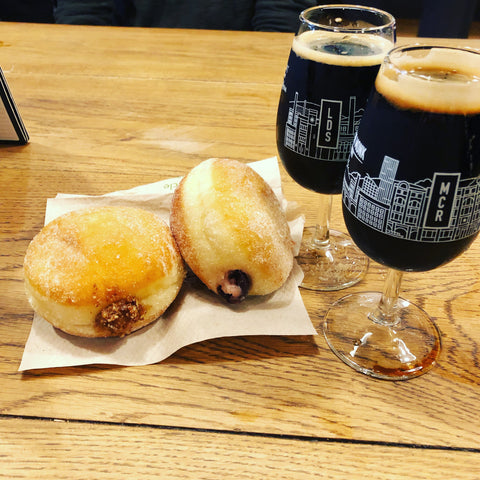 Two doughnuts next to two stouts in one-third glasses.