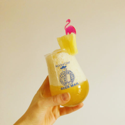 Image of frozen beer slushie in Mikkeller-branded glass with a piece of pineapple and a pink plastic flamingo.