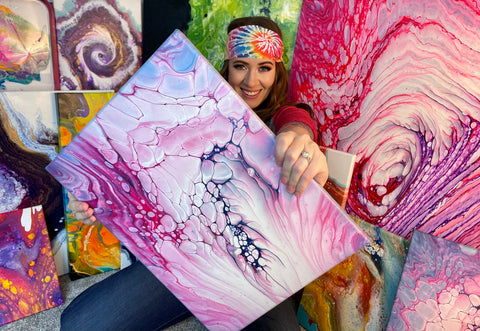 woman holds out colorful pink and purple painting with bubbles in it. She is wearing a colorful JUNK headband and surrounded by her art.