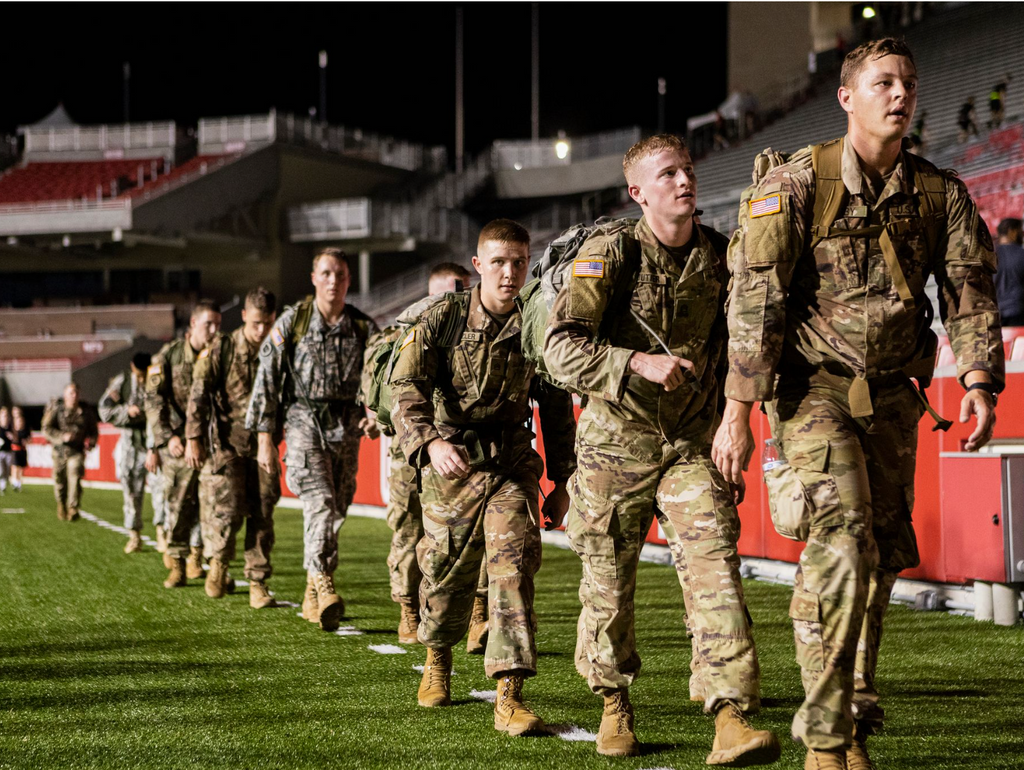 Men walking in a line on the football field dressed in their uniforms.