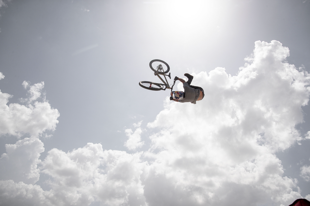 Wild trick from a mountain biker at bike fest in Bentonville - the biker is in the air and the sky is bright behind him as he does a trick where his legs come off the pedals