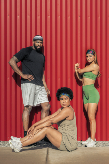 A male athlete and two female athletes wearing JUNK Headband's summer trending collection posed in front of a red metal wall.