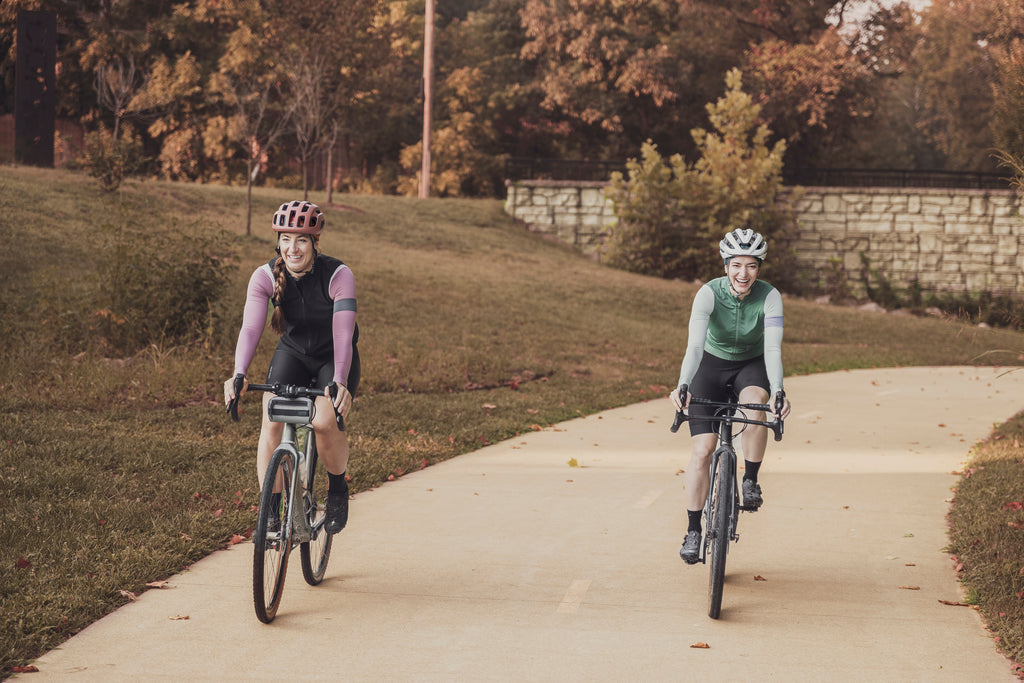 Two women ride towards the camera on a fall day wearing lavender and turquoise in the fall