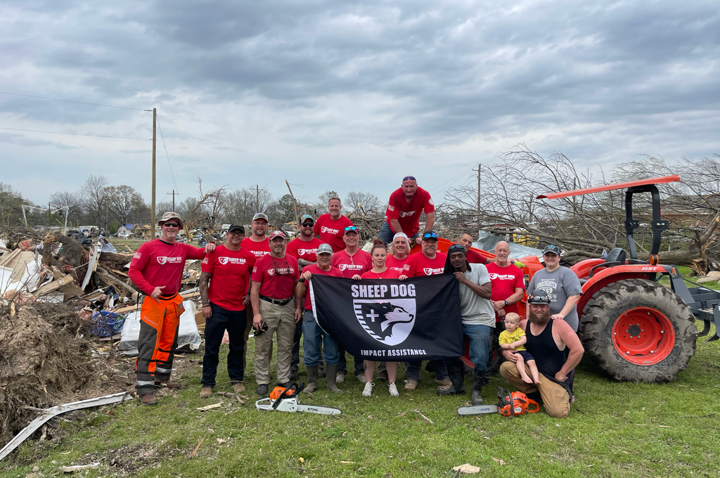 Sheep Dog Volunteers at a cleanup site with a tractor, the sheepdog flag, and behind them is a disaster area