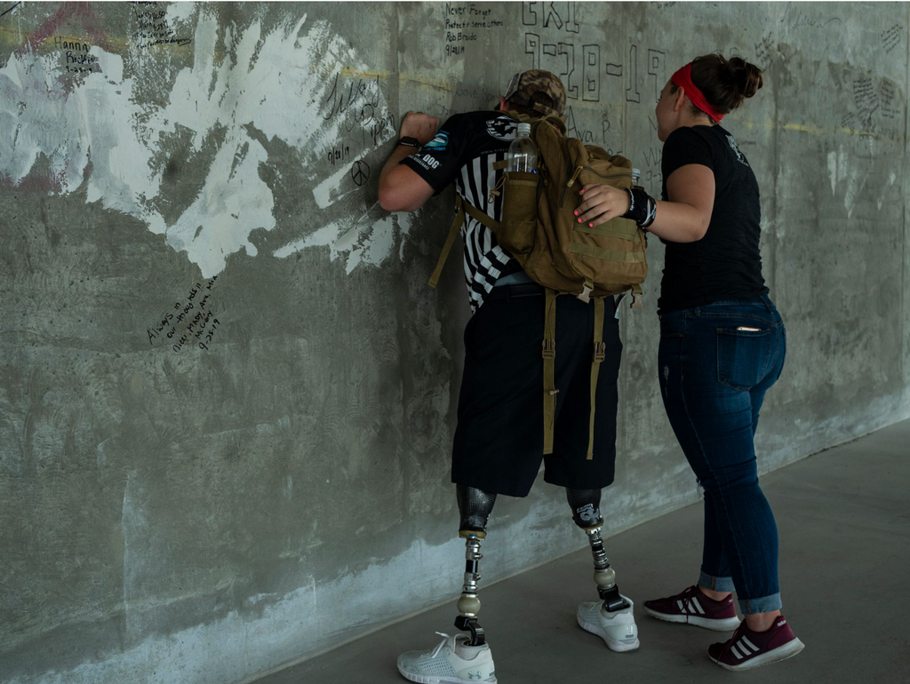 Warrior signs a wall with his wife. The man is an amputee and wears a striped shirt.