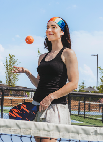 Brown haired woman holding a pickleball paddle and ball at a court ready to play