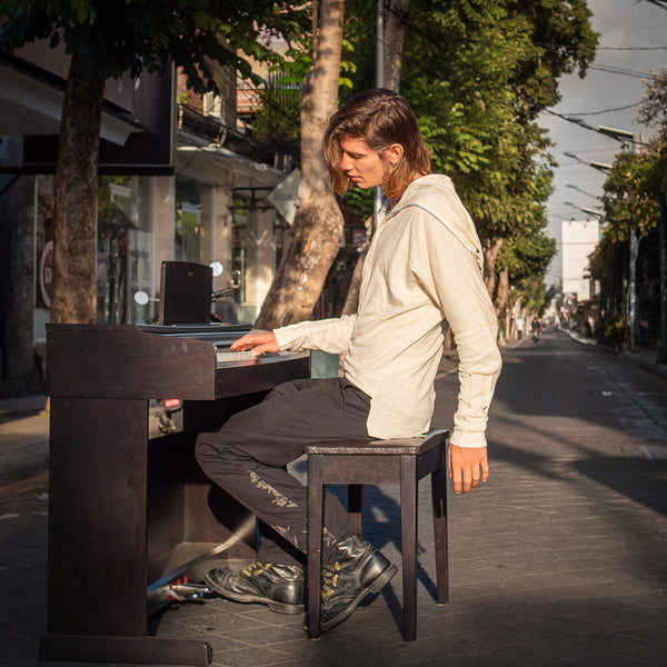 A guy playing piano in middle of empty street wearing psylo fashion unisex clothes