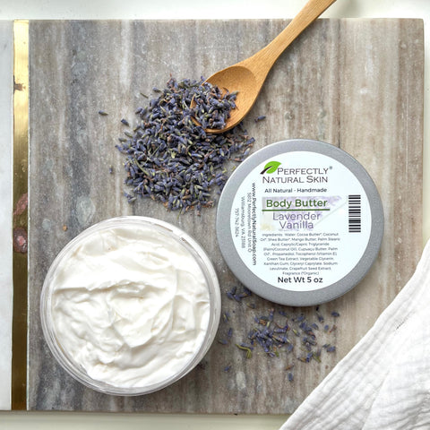 Image of Perfectly Natural Skin Lavender Vanilla Body Butter opened to show the texture.  Jar is among scattered lavender buds.