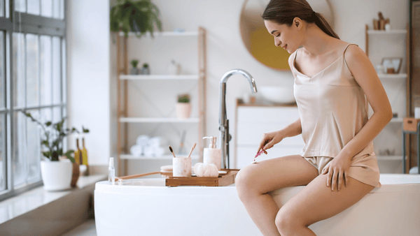 Woman sitting on edge of tub shaving leg