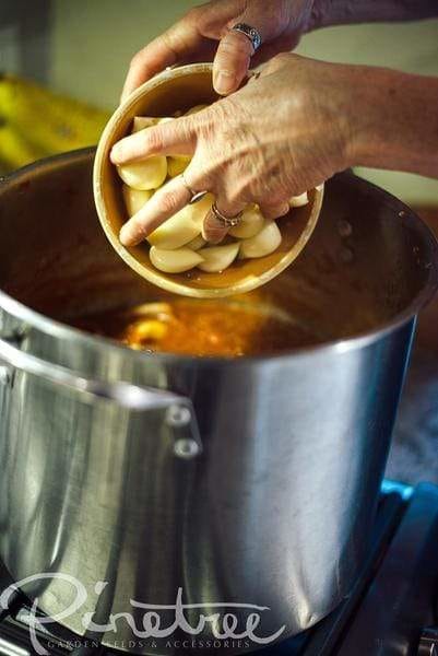 hands pouring garlic from a bowl into sauce in a pot