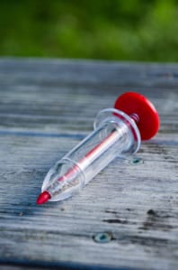 Small, clear seed planting tool with red handle.