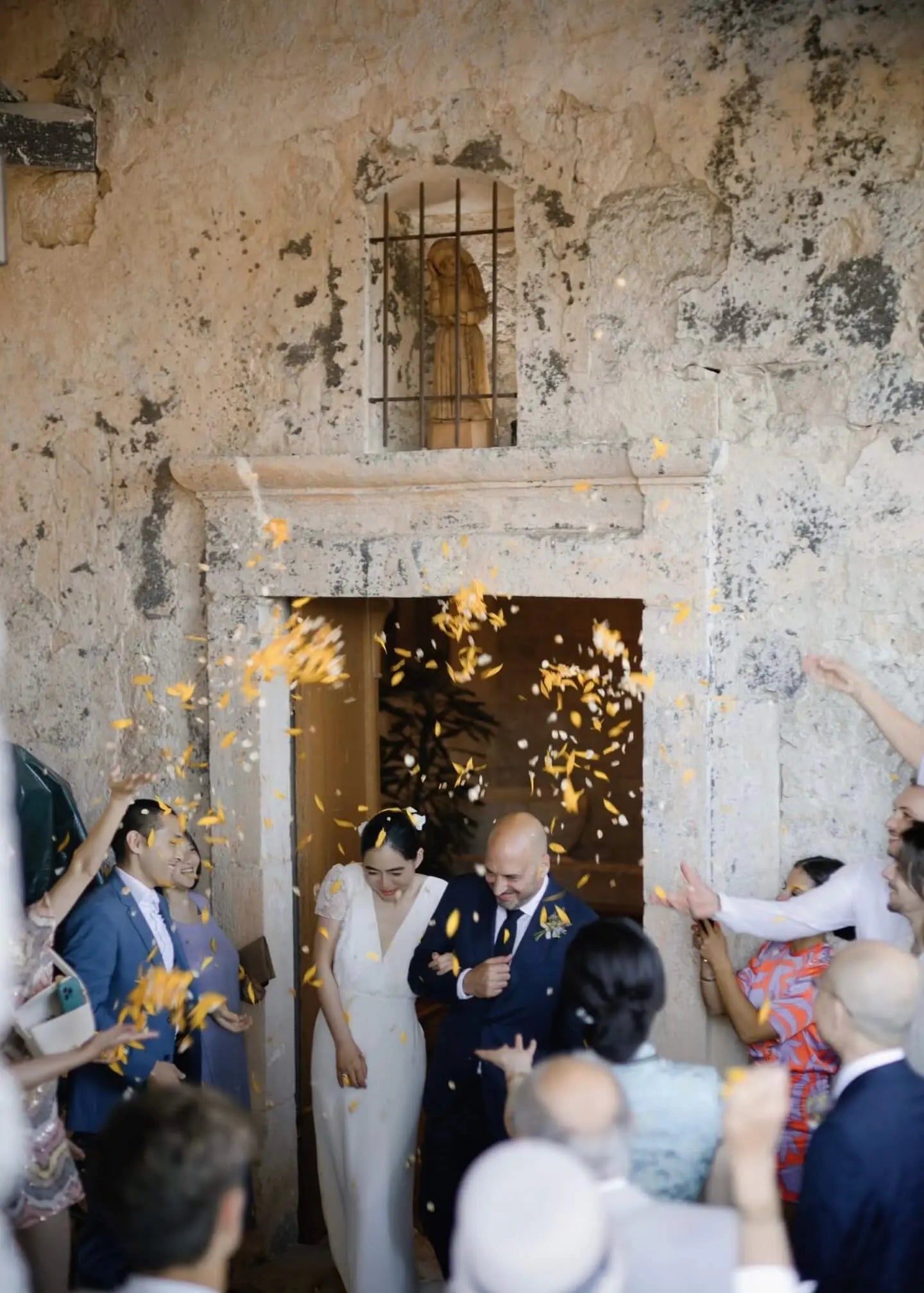Sortie des mariés d'une église champêtre avec confettis dorés et invités joyeux