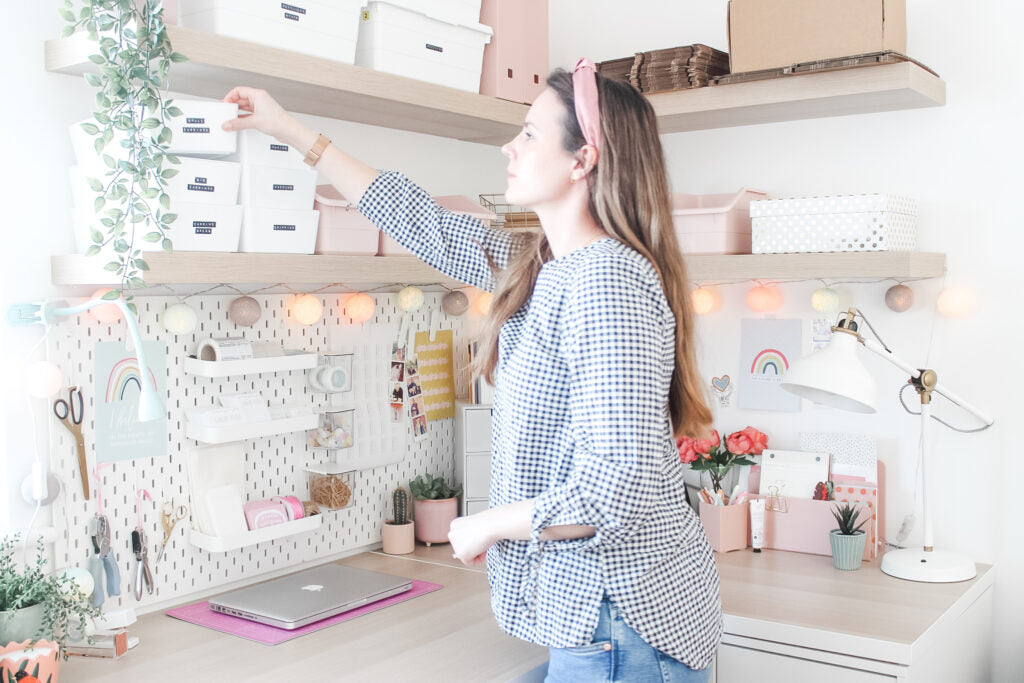 Jade from Ginger Pickle in her pretty and light studio, reaching over to get a box from one of her shelves