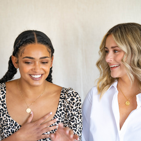 Two models laughing and wearing the gold vermeil shorthand coin pendant necklaces in Love is Love and Thrive 