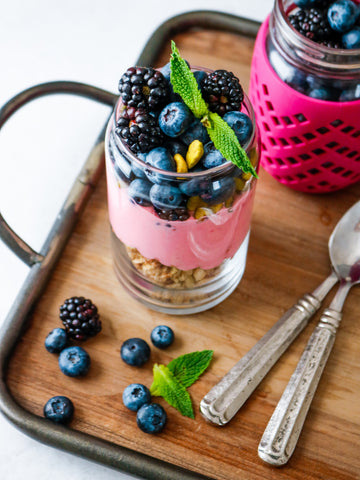 Two mason jars with yogurt, granola, and berries garnished with mint.