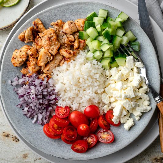A plate with chicken, rice, feta cheese, cucumbers, tomatoes, and red onions arranged in sections.
