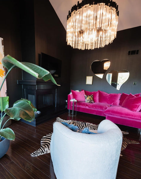 A living room with a black fireplace, pink couch, zebra rug, Varaluz Matrix Pendant Light, Varaluz heart mirrors, against black walls