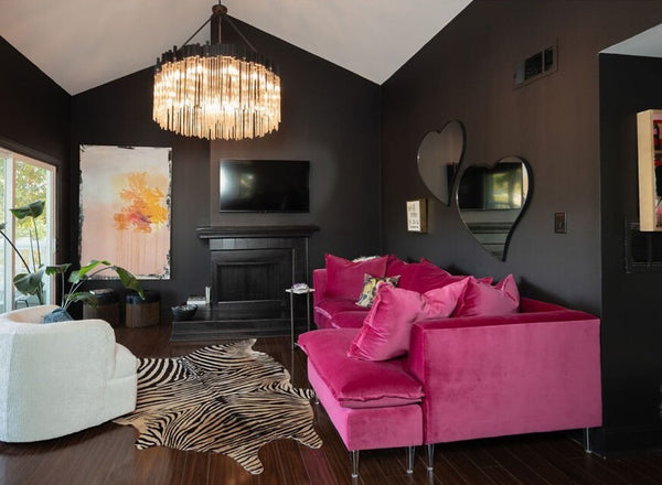 A living room with a black fireplace, pink couch, zebra rug, Varaluz Matrix Pendant Light, Varaluz heart mirrors, against black walls