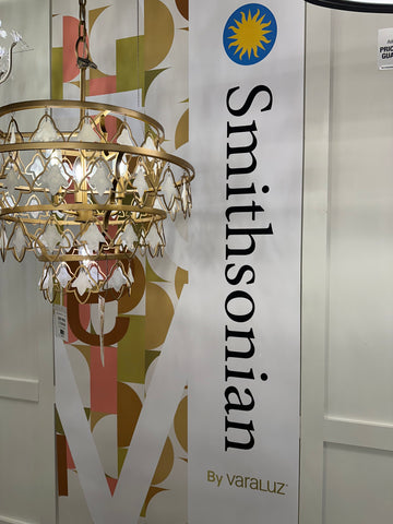 Varaluz gold Fleur chandelier hanging in front of a Smithsonian wall hanging at a lighting showroom