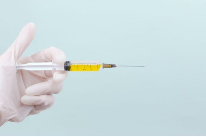 A doctor's hand holding a syringe with yellowish type medicine in it