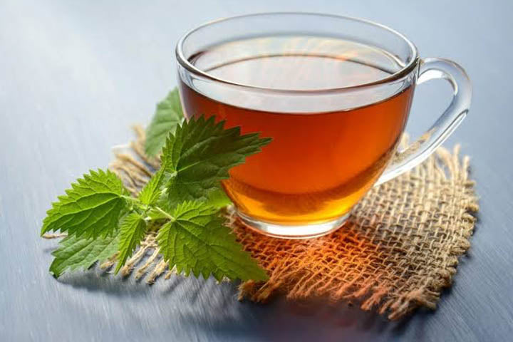 A glass teacup with tea and mint leaves besides it