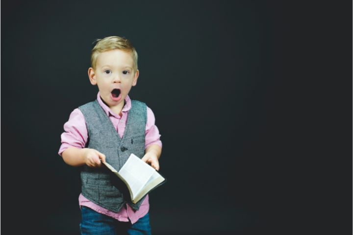 A small kid in jacket and pink shirt a cute emotion of shock holding a book in his hands