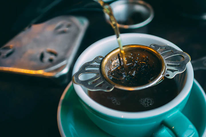 Dandelion tea being poured into a tea cup through a beautiful strainer