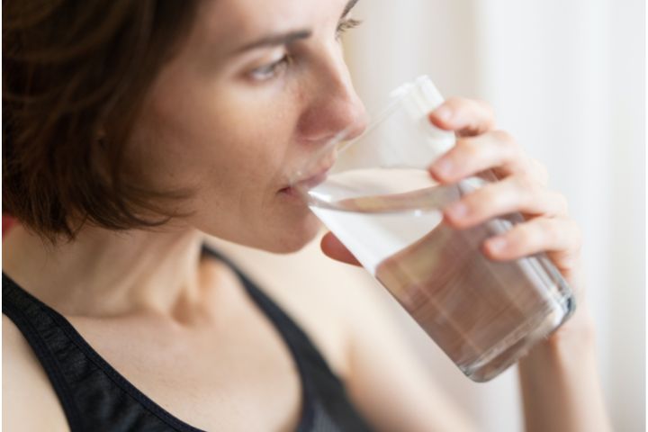 A portrait in a landscape format of a woman in tank top drinking water from a glass