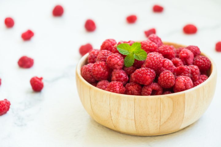 Red raspberry fruits in a small wooden bowl