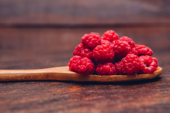 Red Raspberries in a Wooden Spoon Side View on a Wooden Background