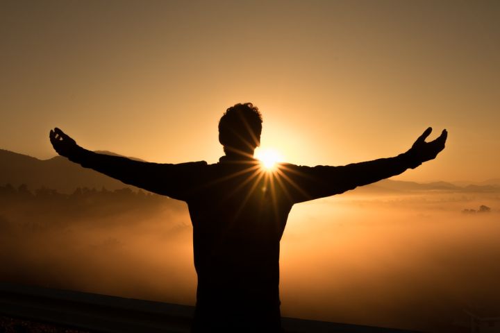 A shadowy photo of a man in sunset opening his arms with the emotion of relief and joy