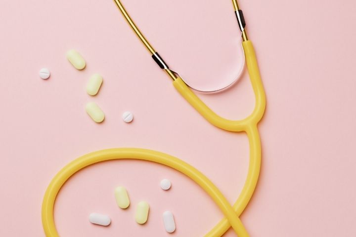 Yellow stethoscope and medicines on a pink background