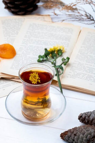 a cup of dandelion tea beside a novel and a dandelion flower