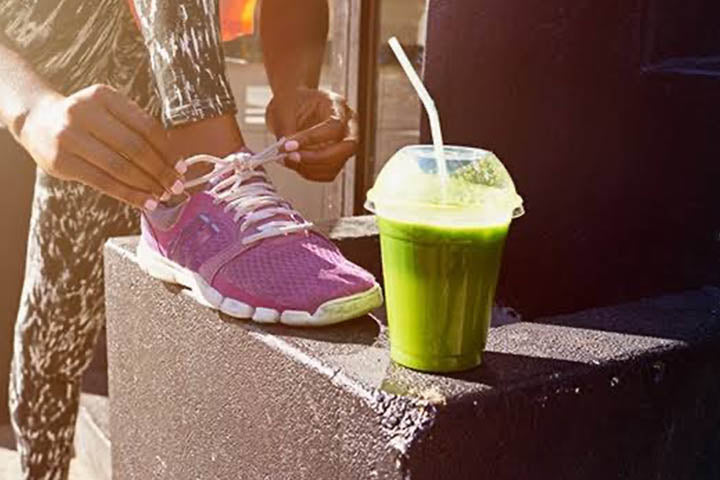 a person tying up their shoelace before drinking a cup of green juice