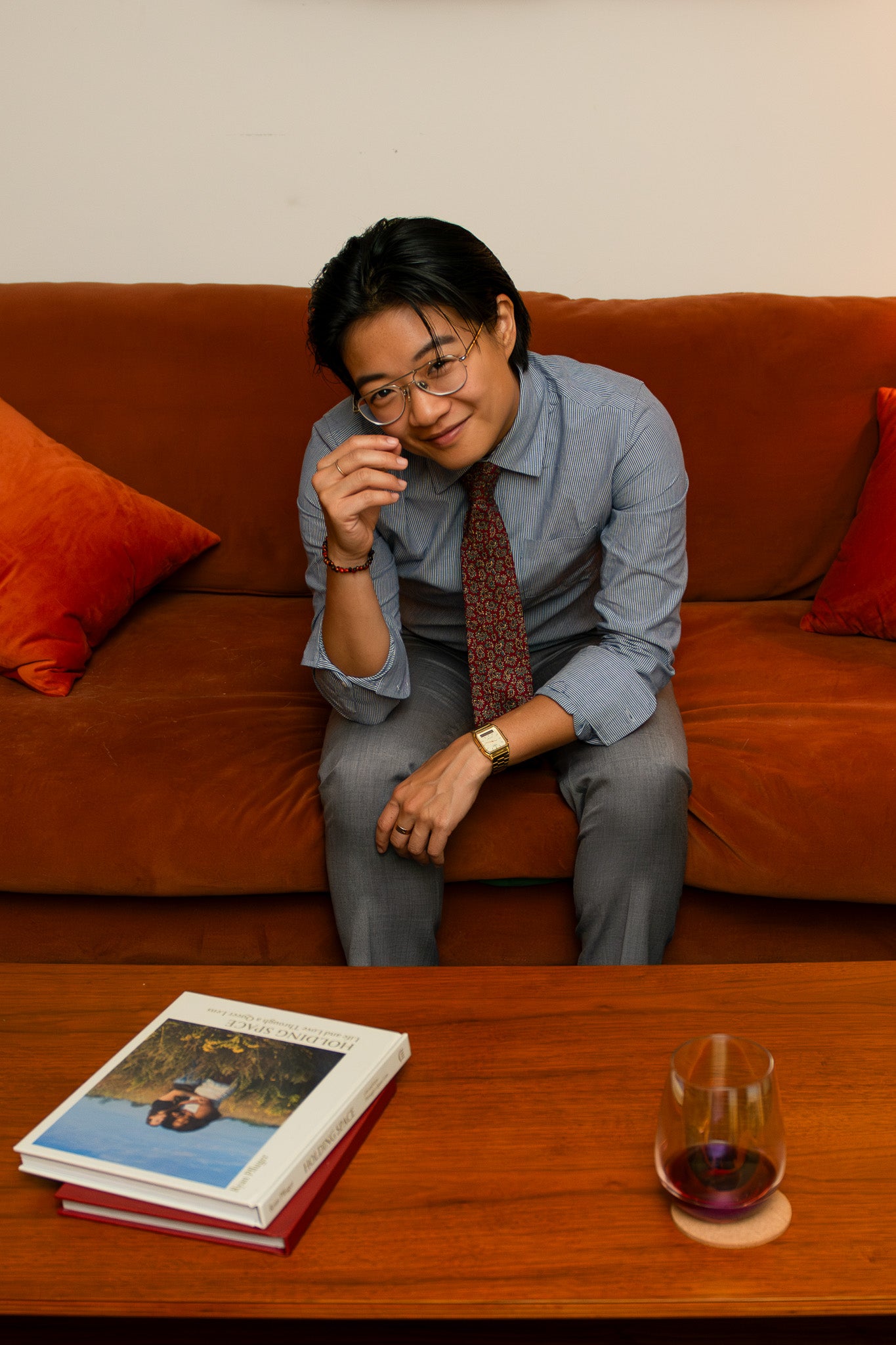 Airin Yung, a transmasculine lawyer sits on an orange velvet couch looking towards the camera with a smile