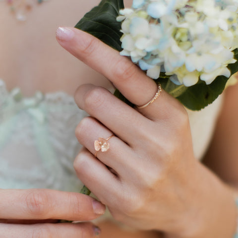 Delicate botanical gold rings by J'Adorn Designs on a white woman's hand, holding a blue hydrangea bloom.