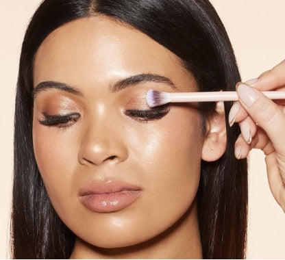 A women with dark hair and flawless skin having shimmer eyeshadow applied using a blending makeup  brush
