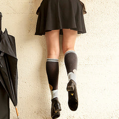 Traveler in skirt and heels leaning over wall wearing grey compression socks with overlapping heart pattern in neutrals