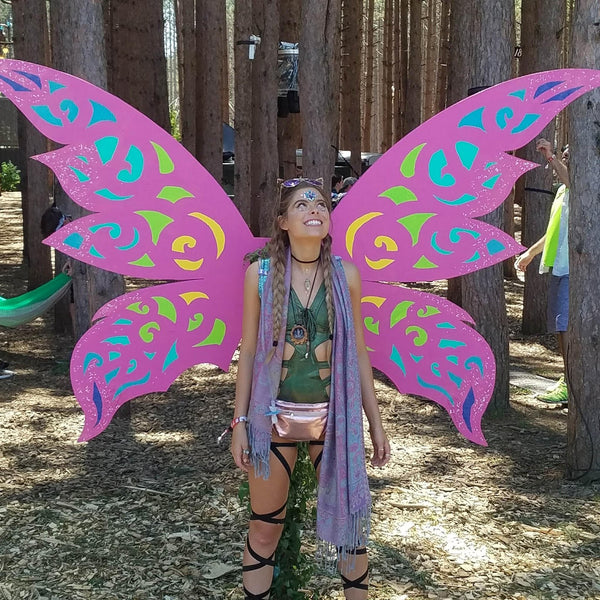 Girl wearing green top and black leg wraps in front of pink butterfly wings at Electric Forest