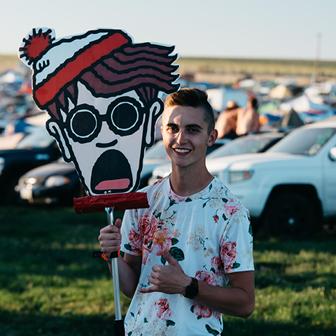 Raver wearing Men's all over print tee with floral pattern and holding a Where's Waldo Totem 
