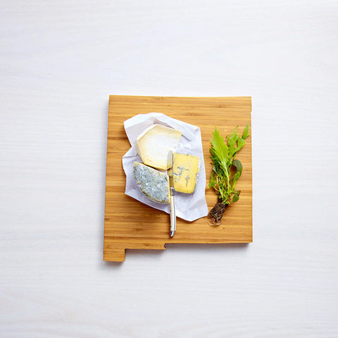 A New Mexico-shaped American Heirloom State-Shaped Cutting Board, decorated with food.