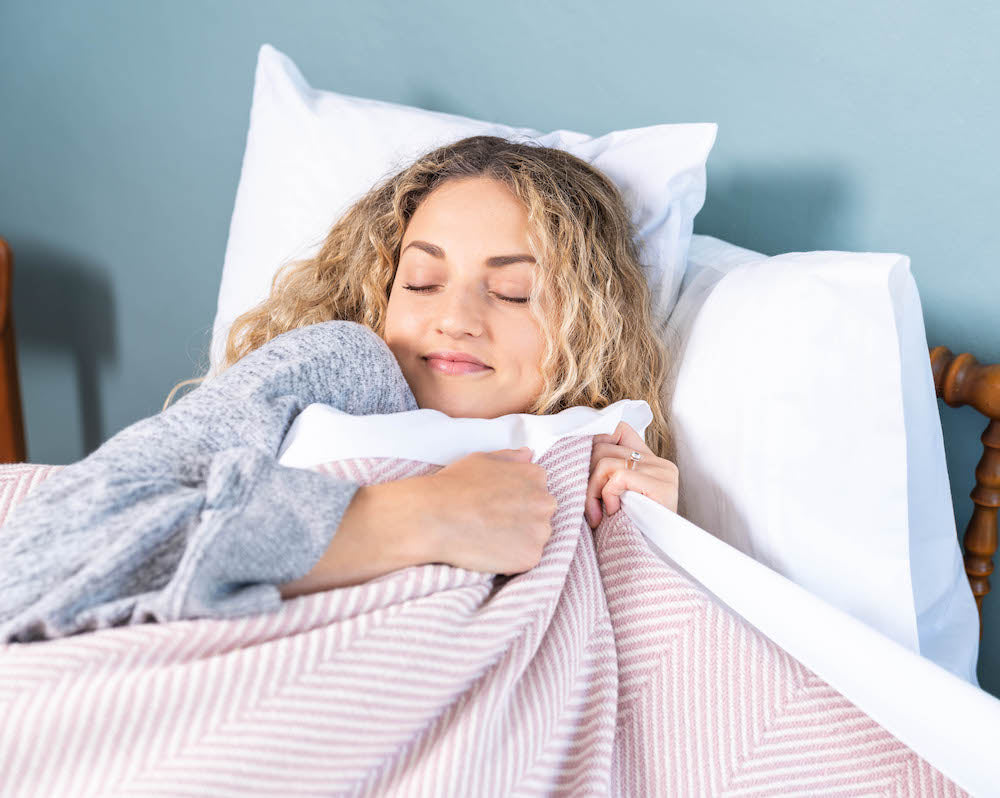 Woman cuddling up tight with blanket sleeping on a made in USA pillow.